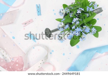 Forget-me-nots in a tine watering can with blue and pink ribbons.