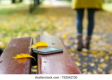 Forgotten Smartphone On A Park Bench. Woman Is Leaving From A Bench Where She Lost Her Cell Phone.