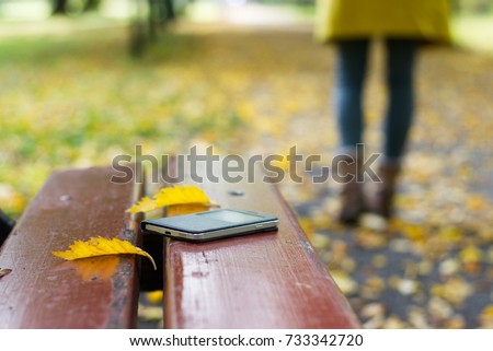 Forgotten smartphone on a park bench. Woman is leaving from a bench where she lost her cell phone.