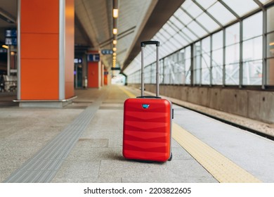 Forgotten travel bag on the train station. Red suitcase on empty station platform. Travel and vacation theme background. Travel banner