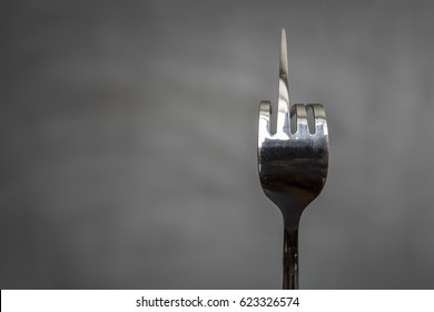 Fork Bent In The Form Of An Obscene Gesture Sign Of The Middle Finger On A Blurred Gray Background