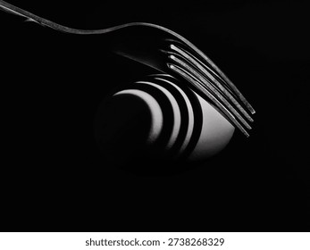 Fork casting dramatic shadow over egg on black background, conceptual still life photography.