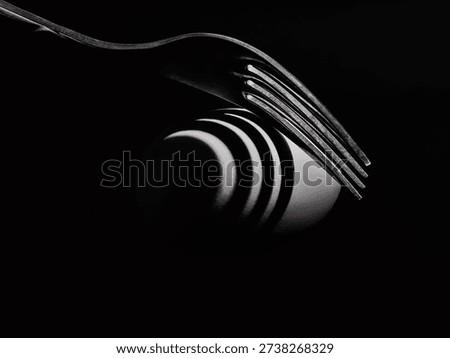 Fork casting dramatic shadow over egg on black background, conceptual still life photography.