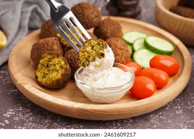 Fork with delicious falafel balls, sauce and vegetables on grunge background, closeup
