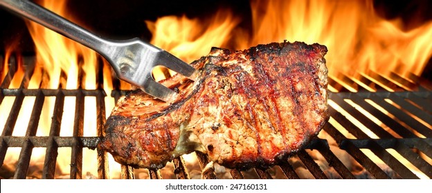Fork in Grilled Pork Chop on  BBQ Grill, Flames of Fire on the Black Background.