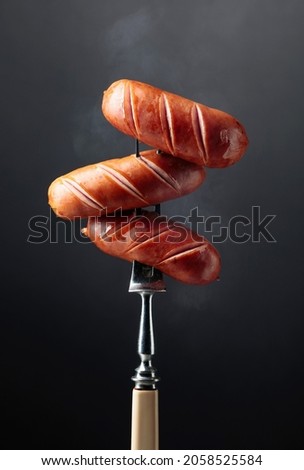 Fork with hot grilled sausages on a black background. 