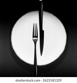 A fork and knife are aligned vertically on a circular white plate, creating a dramatic composition with high-contrast lighting and sharp shadows.