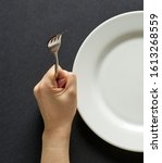 Fork and knife in hands on black background with white plate.