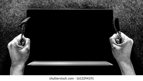Fork and knife in hands on black background with black rectangular plate.