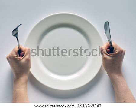 Fork and knife in hands on white background with white empty plate.