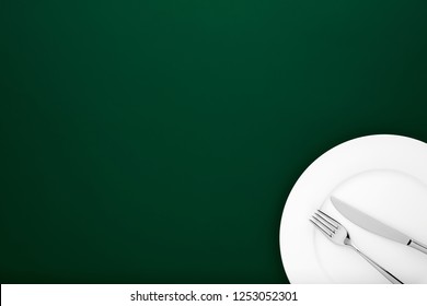 Fork And Knife On White Round Ceramic Plate On Dark Green Background With Copy Space. Top Down View. 