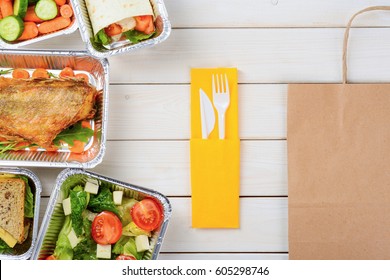 Fork And A Knife, A Paper Bag On The Wooden Surface. Tomato And Lettuce Salad, Sandwiches, Fish, Vegetable Roll, Baby Carrots And Sliced Cucumber. Tasty Meal Delivery.