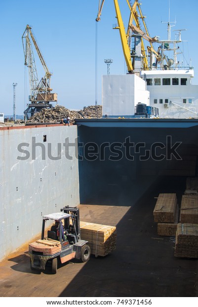 Fork lift truck loading stacked wood planks\
ready for transportation in the ship\
hold