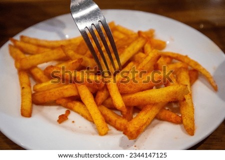A fork was picking up spicy chili powder-flavored fries on white plate