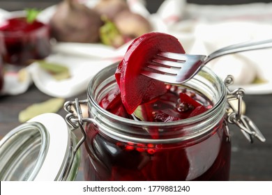 Fork with pickled beets over glass jar on wooden table, closeup