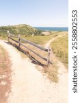 A fork in a sandy trail in the Cape Cod National Seashore, Massachusetts. One trail leads through the dunes, the other to a coastal cottage. A split rail fence separates them. Blue skies in the summer