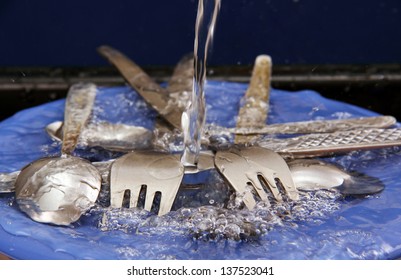 fork, spoon and table knife on blue plate under running water.