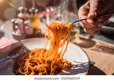 A fork twirls freshly cooked spaghetti bathed in tomato sauce, creating a delightful, sunlit dining experience outdoors. Perfect for Italian cuisine lovers and casual outdoor meals. - Powered by Shutterstock