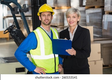 Forklift Driver And His Manager Smiling At Camera In A Large Warehouse