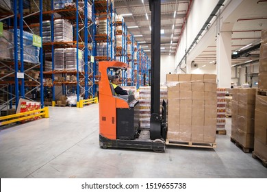 Forklift driver moving packages. Industrial worker in protective uniform operating forklift in big warehouse distribution center. Warehouse worker organizing unloading.
