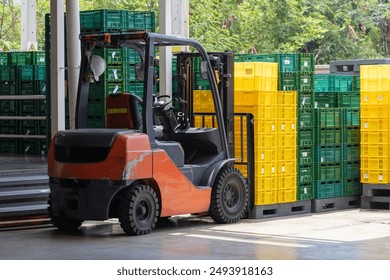 A forklift is driving through a warehouse full of green and yellow boxes. The forklift is orange and black - Powered by Shutterstock