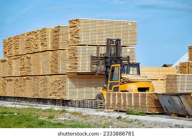 Forklift loading lumber wood boards in stack, finished product warehouse ready for transportation. Sawn boards stack in row. Worker on loader stack in row wooden boards at sawmill - Powered by Shutterstock