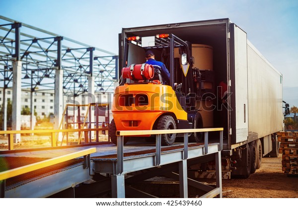 Forklift is putting cargo from warehouse to\
truck outdoors