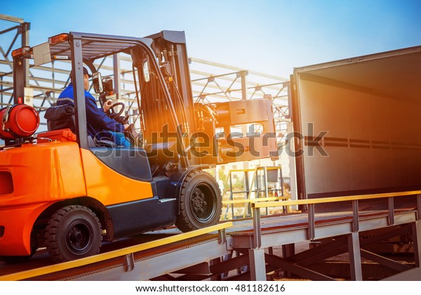 Forklift is putting cargo from warehouse to\
truck outdoors at sunny sky\
background.