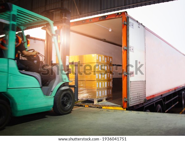Forklift Tractor Loading Package Boxes on\
Pallet into Cargo Container. TrailerTruck Parked Loading at Dock\
Warehouse. Shipment Delivery. Supply Chain. Shipping Logistics\
Freight Truck\
Transportation.