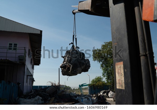 A forklift and workers are lifting an old\
car\'s engine for recycling.