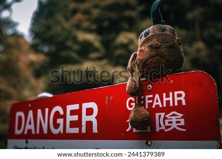 A forlorn stuffed toy rests on a weathered danger sign, an incongruous sight.