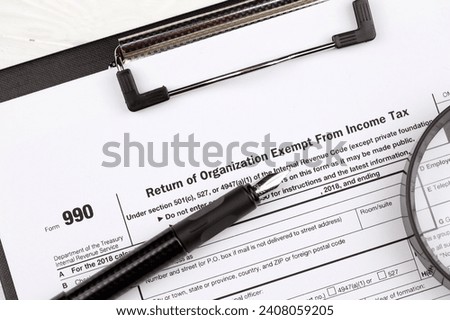 Form 990 Return of organization exempt from income tax on A4 tablet lies on office table with pen and magnifying glass close up