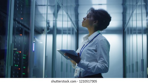 Formal African American woman using tablet while working with server rack in contemporary data center hallway
