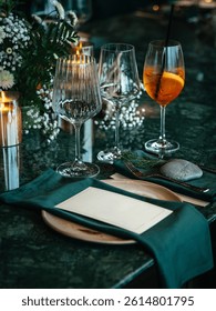  Formal dining table elegantly set with a wine glass, cocktail glass, plates, and green napkins. Florals and candles add a sophisticated touch, perfect for a fine dining experience
