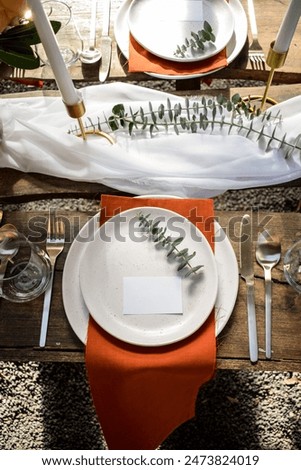 A formal dining table set with plate and cutlery, amid candlesticks and garnishes, with a blank name tag on the plate