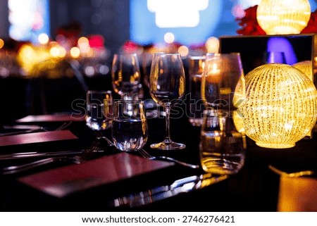 A formal dinner table is prepared with stemware, water glasses, and black linens. A decorative golden orb light serves as a centerpiece.
