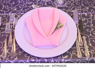 Formal table setting with silverware placed in the order of use, and elegantly wrapped napkin in the shape of a jacket on top of white china, ready for guests at an event, wedding or at a restaurant