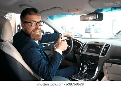 Formal Wearing Young Man Is Sitting In Car, Smiling And Showing Thumbs Up.