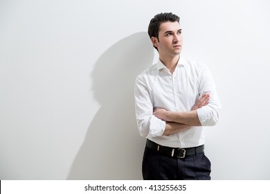 Formally Dressed Caucasian Male With Crossed Arms Standing Against White Wall With Shadow