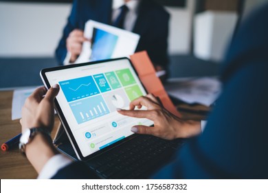 Formally Dressed Faceless Woman Using Tablet Computer Exploring Charts While Sitting At Table In Office During Business Meeting With Colleagues