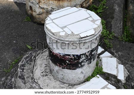 A former paint container repurposed and cemented into a functional seat for relaxing. Showcasing creative upcycling, sustainability, and DIY innovation in everyday objects. Ideal for eco-friendly, recycling, and urban lifestyle themes.