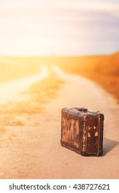 Forsaken abandoned old vintage luggage suitcase on the road fields sky and clouds on the summer sun light - Shutterstock ID 438727621