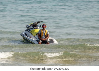 Fort Lauderdale Beach, Florida - USA - February 8, 2021 - Self employee of jet ski business sitting on back of wave runner in ocean water near beach waves wearing safety floatation device vest wet.