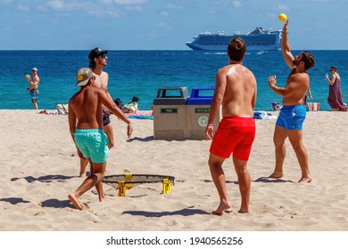 Fort Lauderdale Beach, Florida, USA - March 5, 2021: Sexy visiting fit college tourist menn boys during spring break on the sand playing sports and catching a ball wearing a bathing suit shirtless 