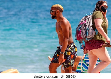 Fort Lauderdale Beach, Florida, USA - March 5, 2021: African American Black Man With Dyed Blonde Short Hair And Dark Beard Wearing Sunglasses And A Bathing Suit On Spring Break Walking On Sand