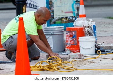 Fort Lauderdale, Florida / USA - 2/27/2019: Construction Worker Installing Concrete Red Block Pavers With Safety Cones, Buckets For Cement, Grout And Yellow Electrical Cables For Power Tools.