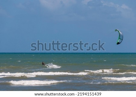 Forte Beach, Bahia - Brazil. Man practicing kite surfing near  Strong wind, sea and sky with different shades of blue and the horizon line on a sunny day.
