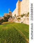 The fortress wall of old Jerusalem. Adorable green lawn growing under ancient walls. Ancient Citadel - Tower of David. Hot summer sunset. The concept of historical, pilgrim and photo tourism