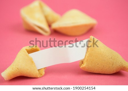 Fortune Cookie on a crimson background. Close-up of foreboding broken cookies with white paper with copy space on a dark pink background