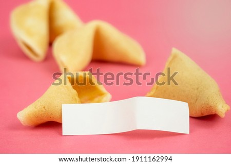 Fortune Cookie on a crimson background. Close-up of foreboding broken asian cookies with white piece of paper with copy space on a dark pink background